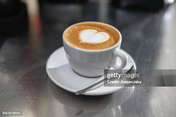 a cup of coffee with a heart shaped latte art placed on a steel countertop - mocha stock pictures, royalty-free photos & images