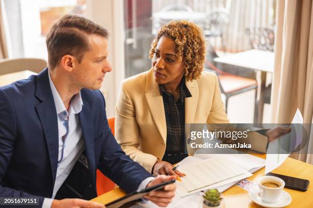 a caucasian businessman and a black businesswoman going over annual reports while at the corporate cafeteria - black white stock pictures, royalty-free photos & images