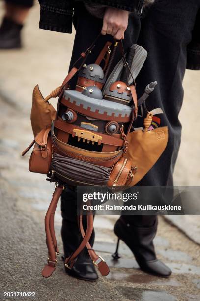 Guest wears black pants, black high heels beige and grey Loewe Moving Castle leather bucket bag outside Loewe during the Womenswear Fall/Winter...