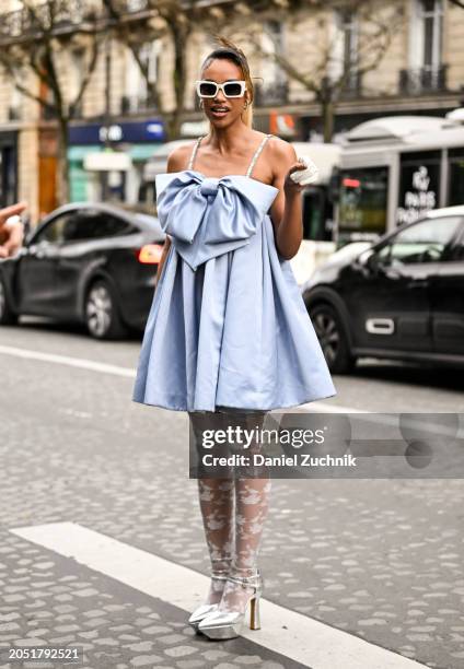 Hanna Lhoumeau is seen wearing a light blue Nina Ricci bow dress, sheer stockings, silver platform heels and white sunglasses outside the Nina Ricci...