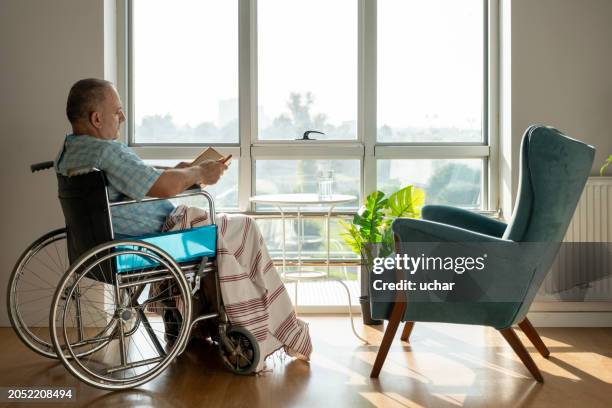 homme mûr lisant un livre dans une chaise handicapée - fauteuil handicap photos et images de collection