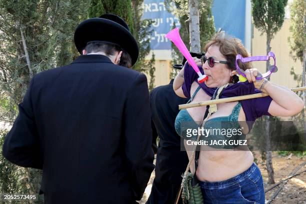 An Israeli protester lifts her T-shirt next to Ultra-Orthodox Jewish men outside an army recruiting office in the town of Kiryat Ono near Tel Aviv on...