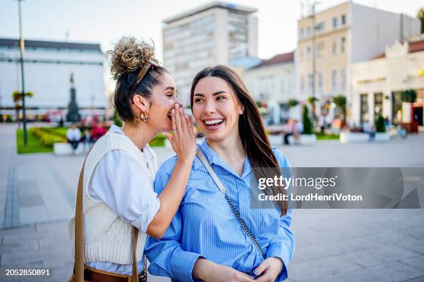woman whispering in the ear of her female friend - whispering stock pictures, royalty-free photos & images
