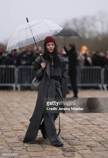 Youo Chao was seen wearing a red hat, a beige bag, a grey long coat, a cropped grey top, pants and black shoes as well as a transparent umbrella...