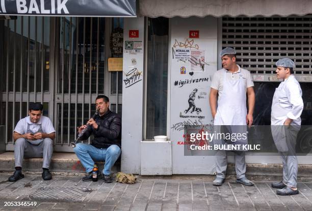 Restaurants workers listen to a street mucisian during their break at Kadikoy in Istanbul on March 5, 2024.