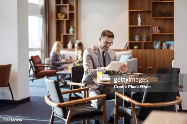 businessman sitting in business lounge and working on digital tablet - entrepreneur stockfoto's en -beelden