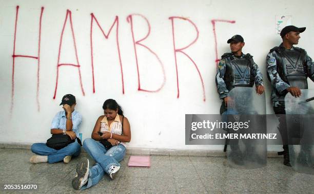 Dos maestras hondureñas permanecen sentadas junto a policias anti-disturbios durante una protesta en reclamo del pago de adeudos salariales, en las...