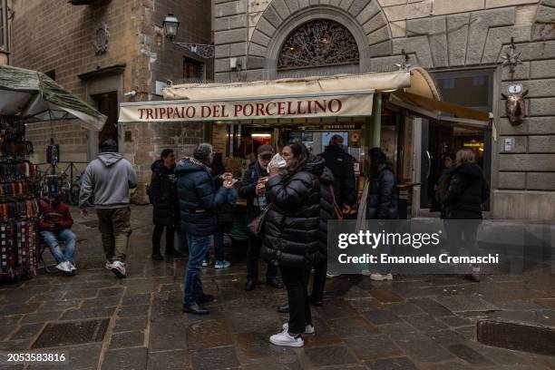 People stand while eating a sandwich with lampredotto - a typical Florentine dish, made from the fourth and final stomach of cattle, the abomasum -...