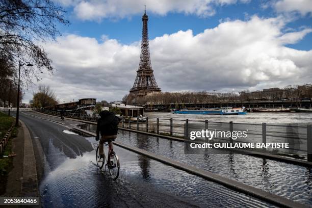 Person rides a bike on the flooded Seine river banks with the Eiffel Tower appearing in the background in Paris on March 5, 2024.