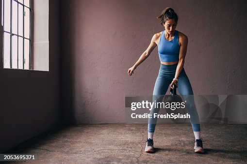 Focused Woman Exercising with Kettlebell in a Gym Setting Focused Woman Exercising with Kettlebell in a Gym Setting