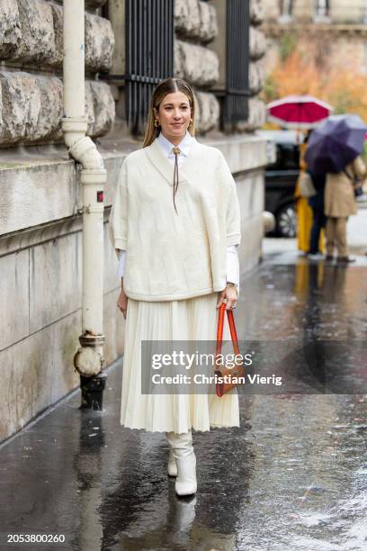 Guest wears creme white pleated skirt, knit, orange bag, white button shirt outside Hermes during the Womenswear Fall/Winter 2024/2025 as part of...