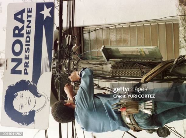 Un trabajador de telecomunicaciones trabaja reparando lineas 28 de Noviembre frente a un cartel con propaganda de la candidata Nora de Melgar en...