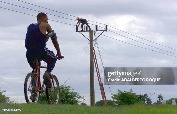 Cuban farmer on his bicycle passes in front of a worker of electricity company who repairs the facilities damaged by the passage of the tropical...