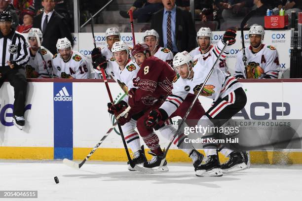 Taylor Raddysh of the Chicago Blackhawks and teammate Anthony Beauvillier battle for possession with Nick Schmaltz of the Arizona Coyotes during the...