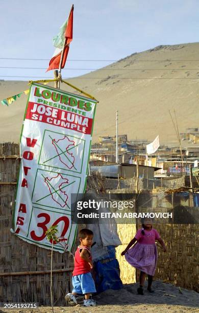 Two children play in the doorway of a straw house in a marginal neighborhood of Lima, Peru, 04 April 2001 next to a politic banner for Lourdes...