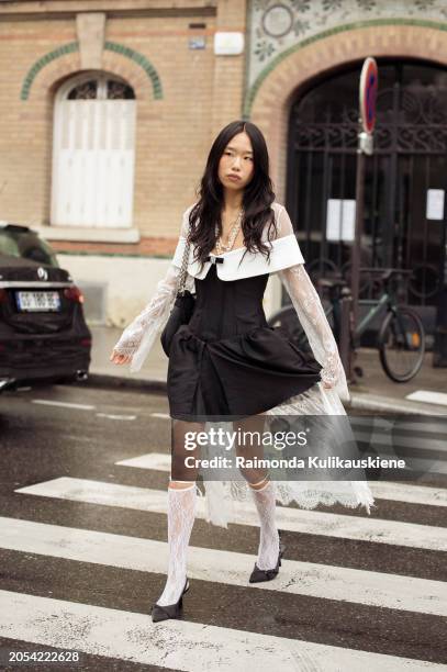 Guest wears black dress with white collar and white lace details, white lace socks and black bag outside Vivienne Westwood during the Womenswear...