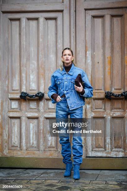 Helena Bordon wears golden earrings, lipstick, a brown turtleneck pullover , a blue oversized denim jacket, blue gathered denim pants / jeans ,...