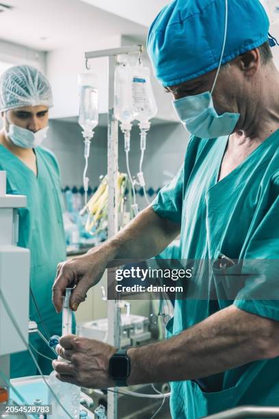 an anesthesiologist administers fluid into the iv drip while a practitioner observes - administers stock pictures, royalty-free photos & images