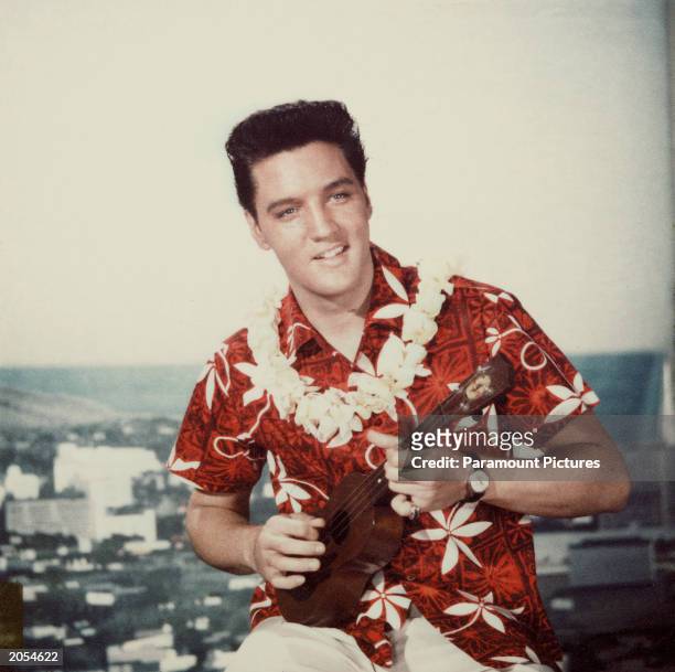 American rock n' roll singer Elvis Presley plays a ukelele, wearing a Hawaiian shirt and lei, in a still from the film 'Blue Hawaii,' directed by...
