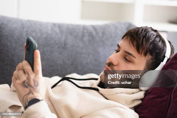 handsome man lying on the sofa listening to music on headphones - lost stock pictures, royalty-free photos & images