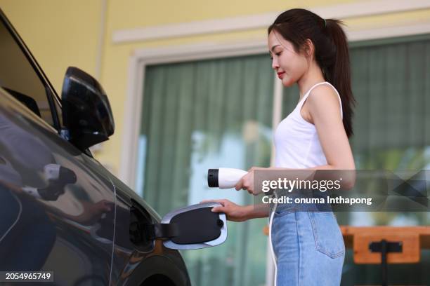 young woman with new electrical car ev car battery charger at home, international women's day - battery charger stock pictures, royalty-free photos & images