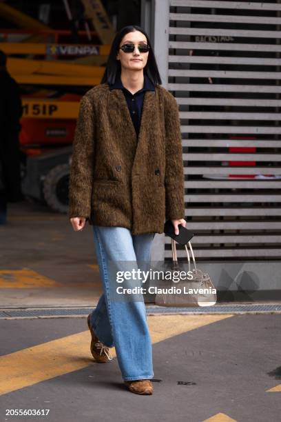 Guest wears blue polo neck top, brown jacket, jeans, cream bag, brown sneakers, outside Ferragamo, during the Milan Fashion Week - Womenswear...