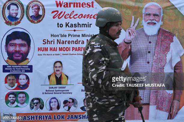 Indian security personnel stands guard infront of a poster with a portrait of Indian Prime Minister Narendra Modi in Srinagar on March 6 on the eve...