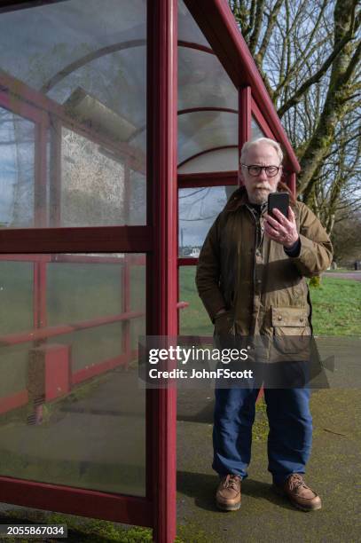 mature man standing alone at a bus stop - waxed jacket stock pictures, royalty-free photos & images
