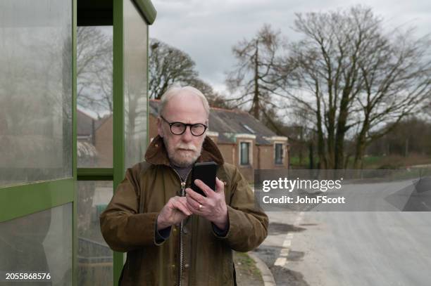 senior man looking at his mobile phone - waxed jacket stock pictures, royalty-free photos & images