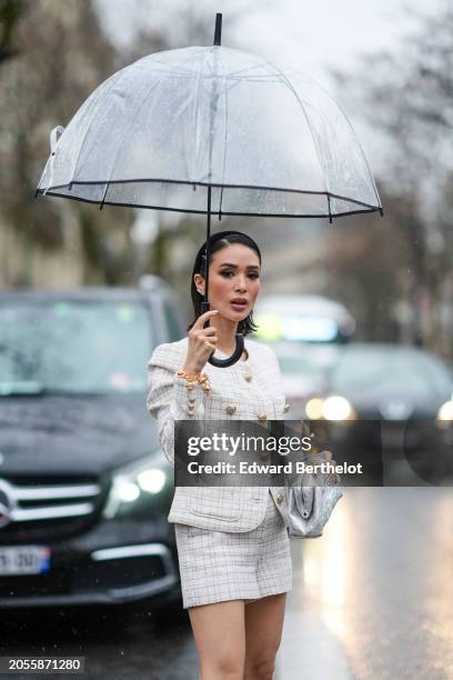 Heart Evangelista wears a headband, earrings, pink lipstick, a white blazer jacket with golden buttons, a golden bracelet, gray shiny pouch bag, a...