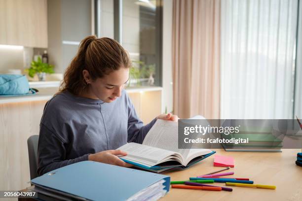 adolescente lisant un manuel scolaire étudiant à la maison - manuel scolaire photos et images de collection