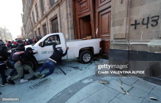 Demonstrators push a pickup truck to break down a presidential palace door in Mexico City on March 6 during a protest over the disappearance of the...