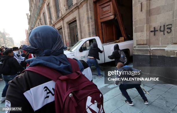 Demonstrators push a pickup truck to break down a presidential palace door in Mexico City on March 6 during a protest over the disappearance of the...