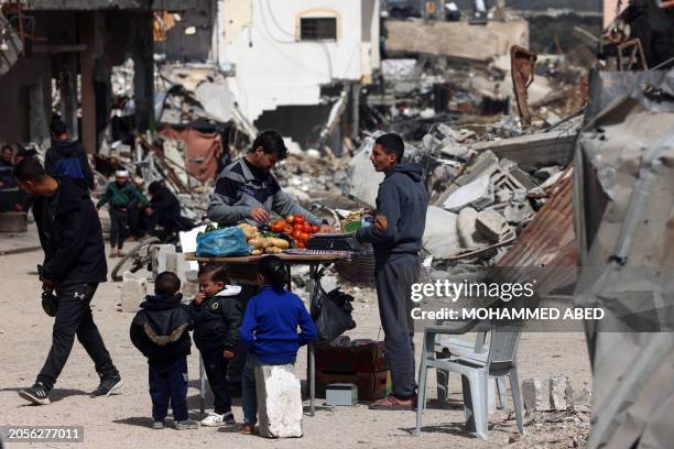 Palestinians buy vegetables from a street vendor's stall next to mounds of building rubble due to Israeli bombardment at the Bureij refugee camp in...