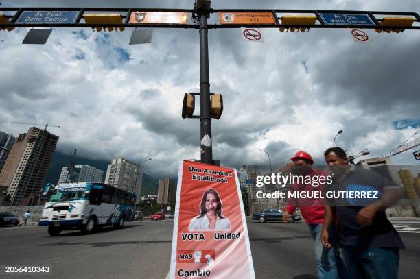 Citizens pass by in front of a pole with a poster of the opposition candidate to the national parliament, Maria Corina Machado, in Caracas on...