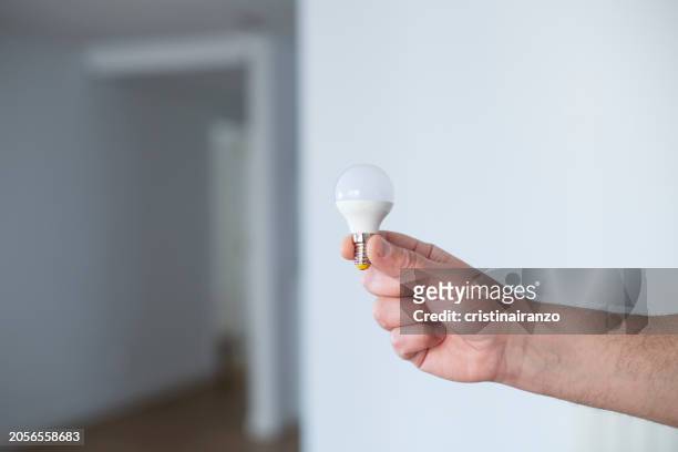 man's hand holding a light bulb - cristinairanzo stock pictures, royalty-free photos & images