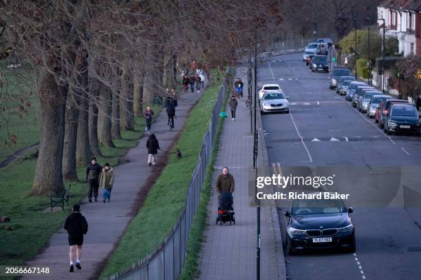 Suburban street lined with residential properties, parked cars and park users walking in Ruskin Park in south London, Lambeth, on 2nd March 2024, in...