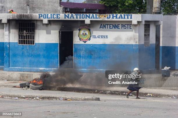 An elderly woman runs in front of the damaged police station building with tires burning in front of it after armed gang members exchanged gunfire...