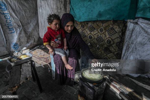 Palestinian Fatma al-Sersek prepares a meal for her child in a tent, where she takes refuge after her uncle's house in Khan Yunis city is destroyed...