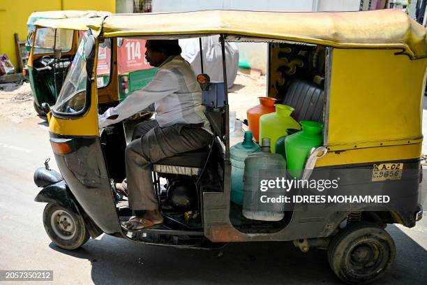 An autorickshaw driver carries empty cans to fill water from a municipal tap, amid an ongoing water crisis in Bengaluru on March 7, 2024.