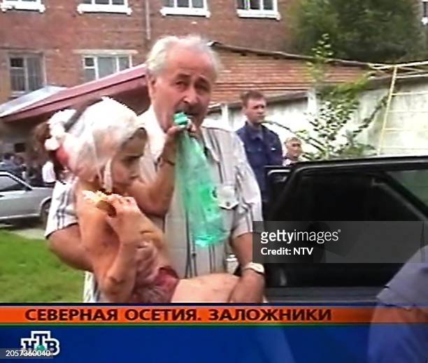 This TV-grab image taken from Russian NTV channel shows as Ossetian man carrying a little girl, after the rescue operation, 03 September 2004 in the...