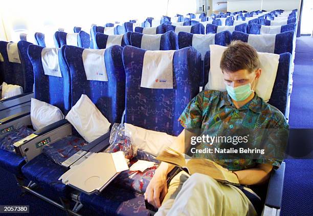 Lone western visitor wearing a surgical mask reads a book in a nearly empty Air China flight from Hong Kong to Beijing on June 5, 2003 in Beijing,...