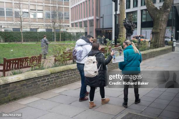 Woman shows another the front page of a tabloid newspaper while walking down a road in SW!, on 6th March 2024, in London, England.