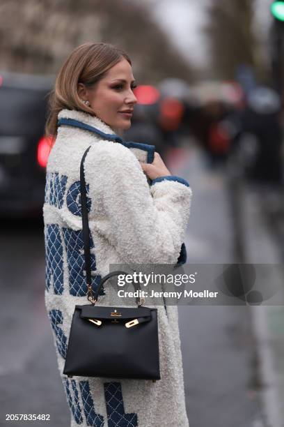 Ginta seen wearing diamond earrings, white / blue fluffy long coat with pearl embroidered quote on the back and Hermès black leather bag, before...