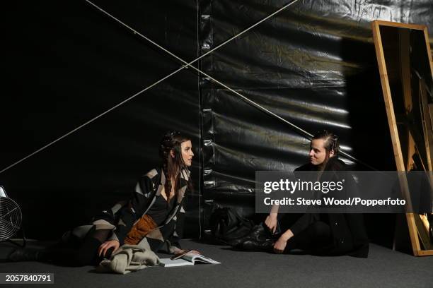 Backstage at the Cividini show during Milan Fashion Week Autumn/Winter 2016/17, two models seated on the floor chatting, one wears a brown suede...