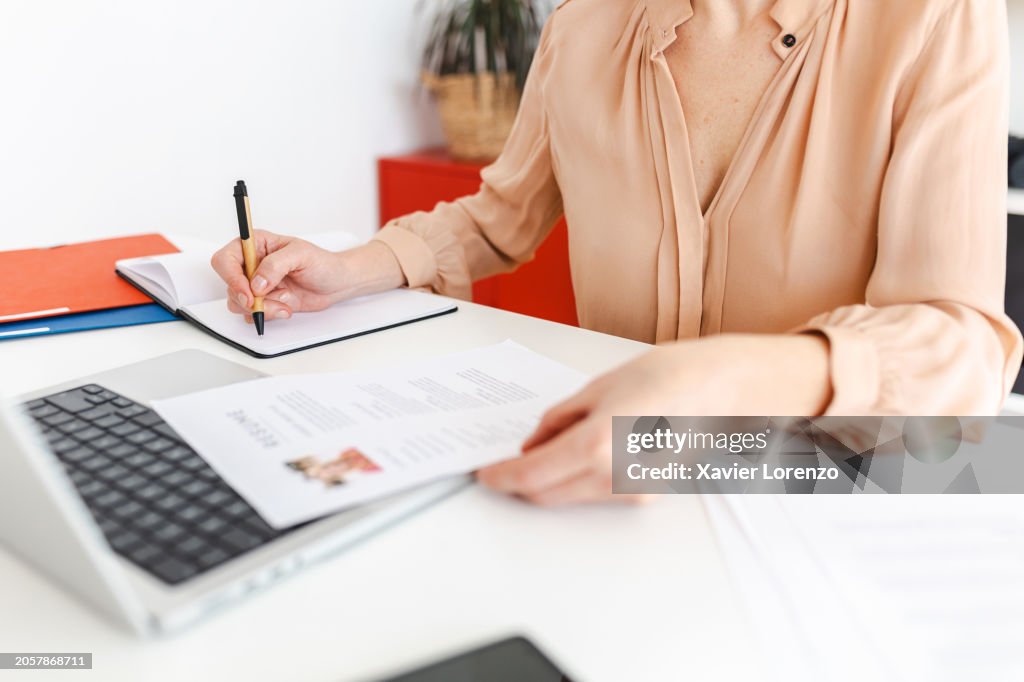 Close up view of female HR recruiter taking notes while reading job applicant resume in the office.