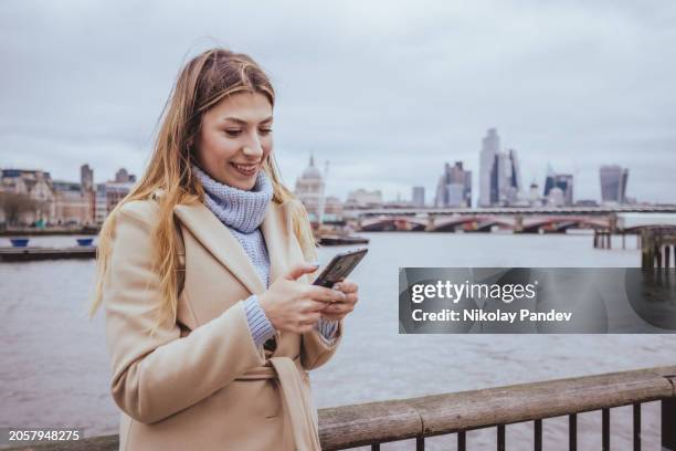 candid waist up portrait of a young cheerful girl in her 30s texting on her smart mobile phone device in down town central city of london, great britain - creative stock photo - greater london stock pictures, royalty-free photos & images