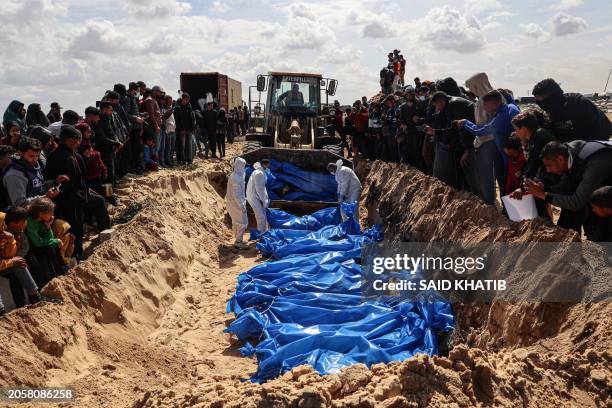 Mourners watch as medical personnel prepare the bodies of 47 Palestinians, that were taken and later released by Israel, during a mass funeral in...