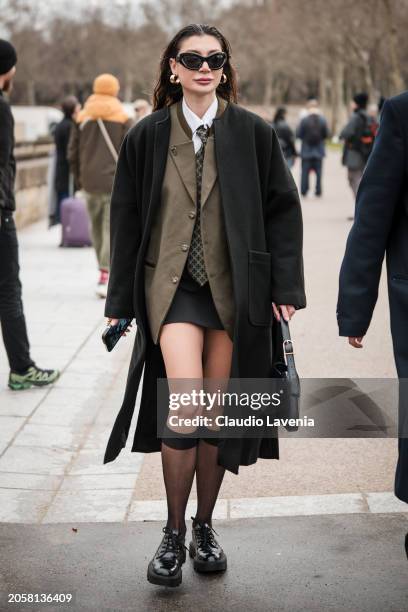 Guest wears olive green blazer, white shirt, printed tie, black coat, black mini skirt, black sunglasses, black bag, black socks, black shoes,...