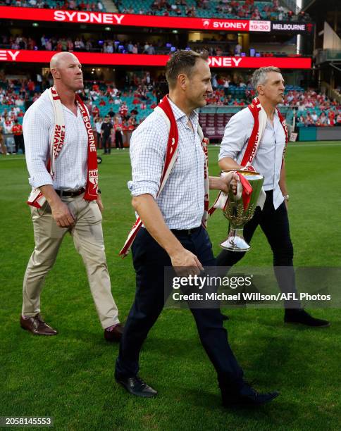 Jude Bolton, Barry Hall and Leo Barry hold the 2005 Premiership Cup during the 2024 AFL Opening Round match between the Sydney Swans and the...